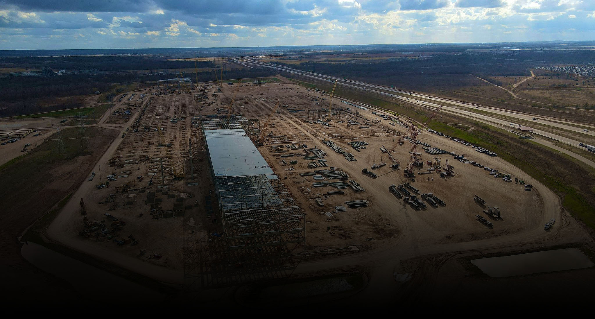 Aerial view of a vast factory under construction, the ground fading to black at the base.